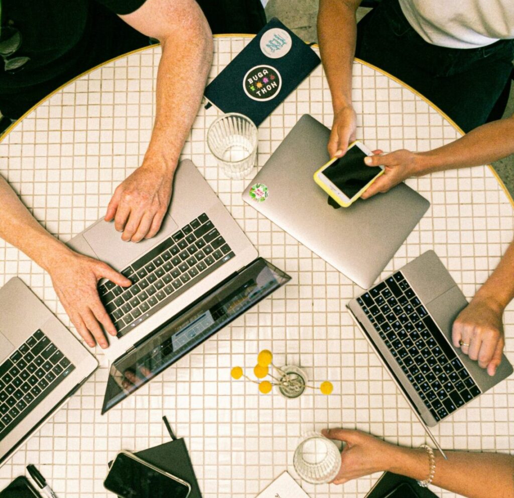 Top view of a team collaborating with laptops, phones, and notes in a modern office.
